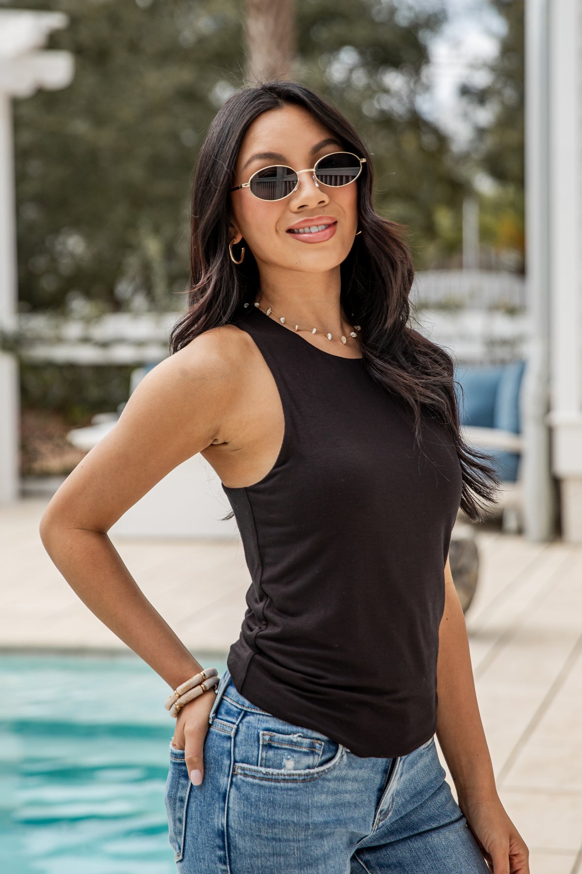 Woman wearing a black tank top and blue jeans by a pool