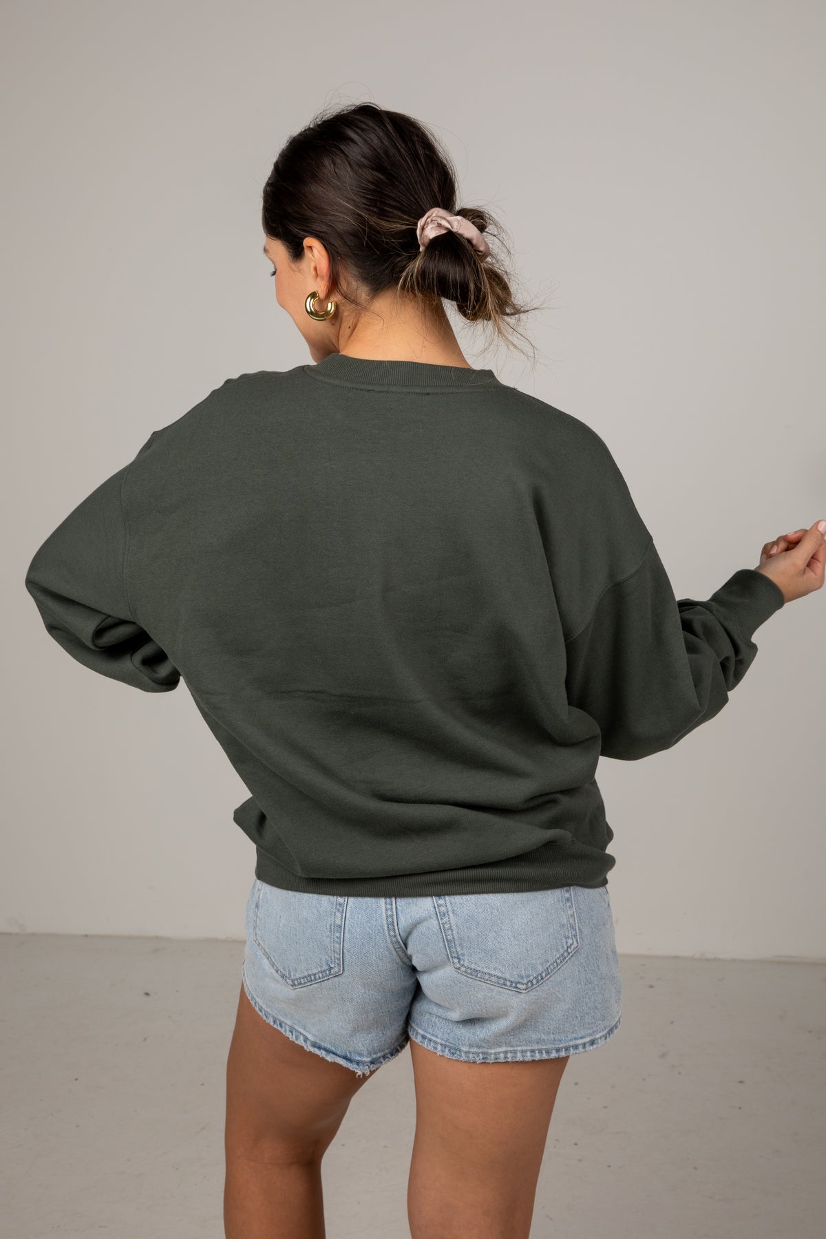 Person wearing a green sweatshirt and light blue shorts against a plain background