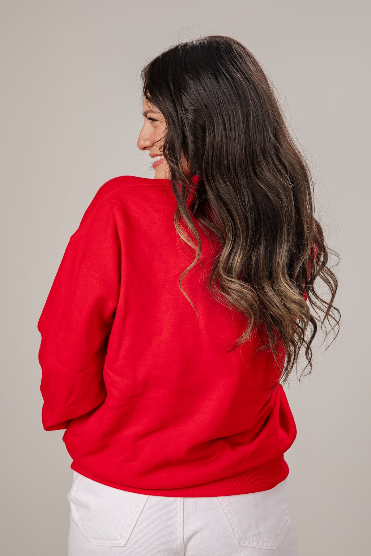 Woman wearing a red sweater and white pants against a plain background