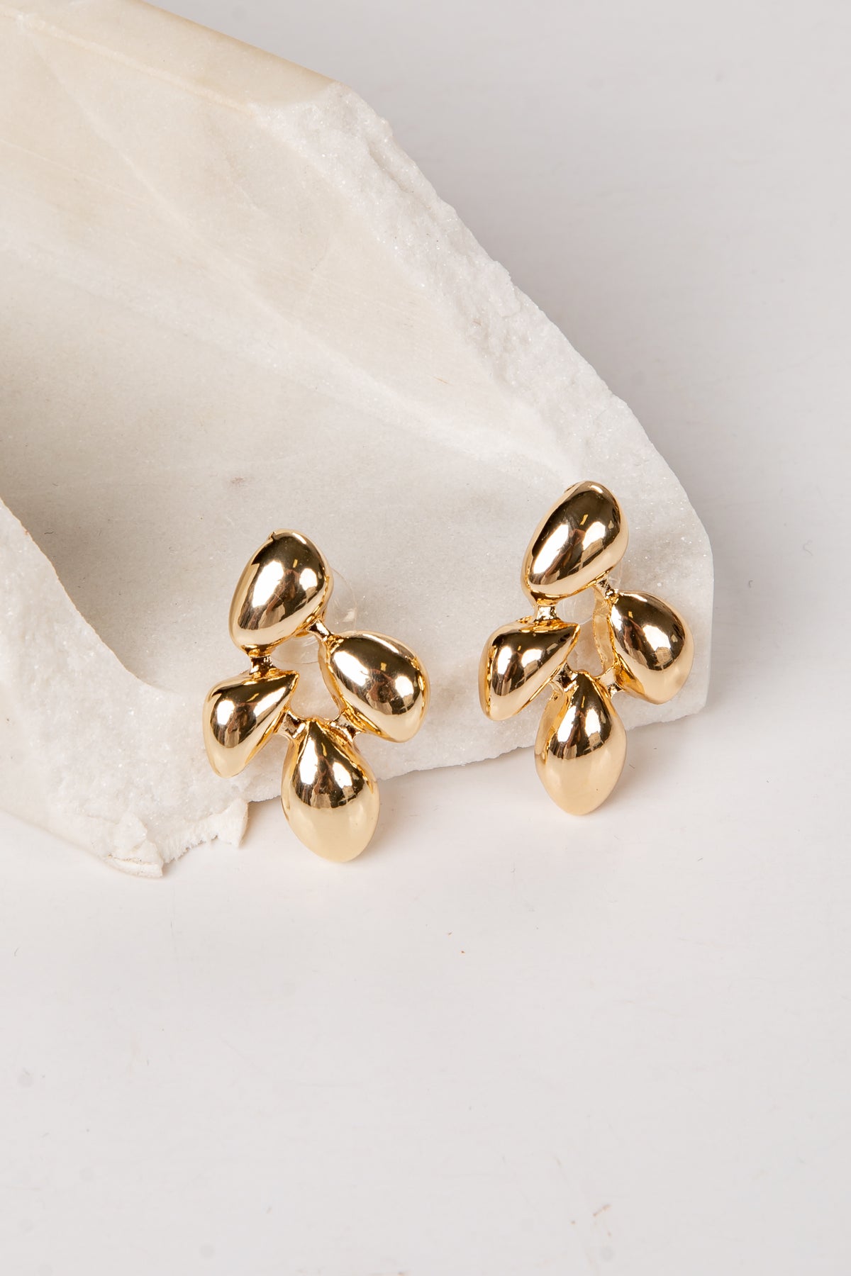 Gold leaf-shaped earrings on a white fabric background