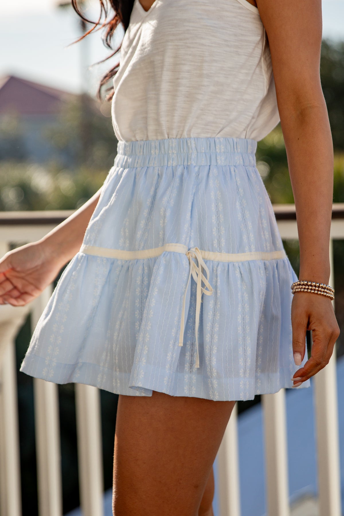 Person wearing a light blue skirt with a white top, standing outdoors.