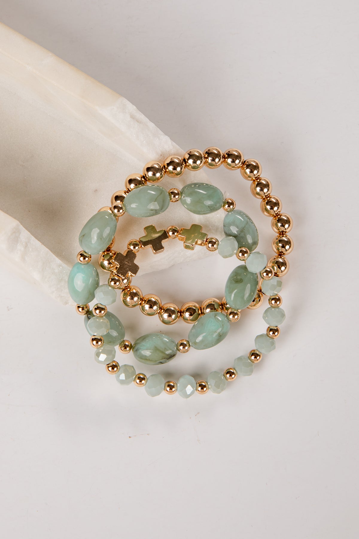 three bracelets with green beads and gold accents on a light gray background