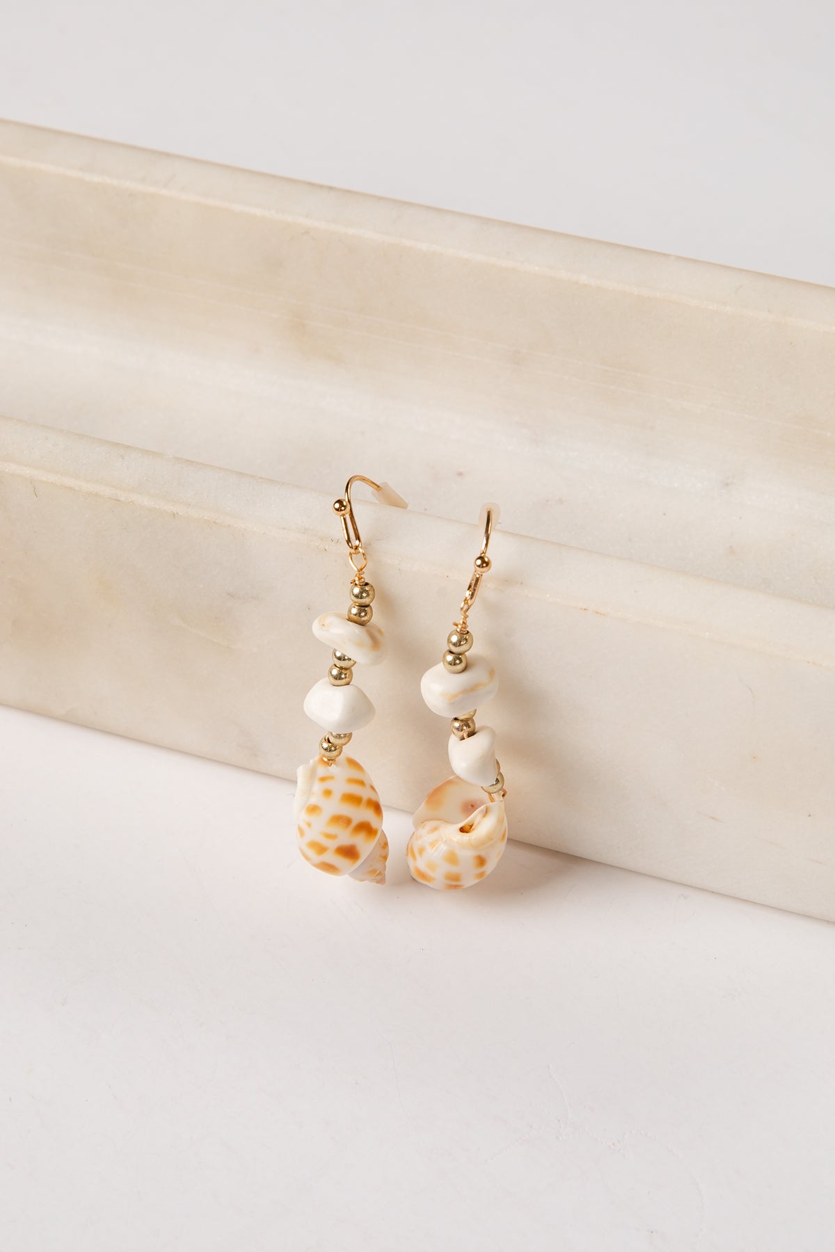 Shell and pearl earrings on a textured beige surface