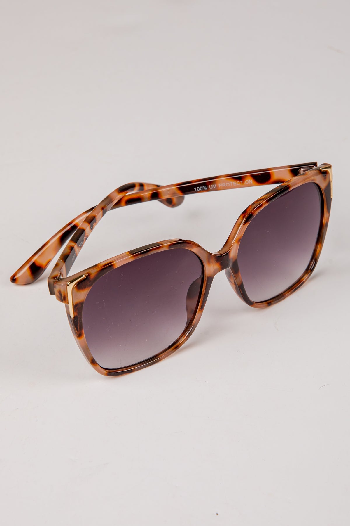 Sunglasses with tortoiseshell frame and dark lenses on a light gray background