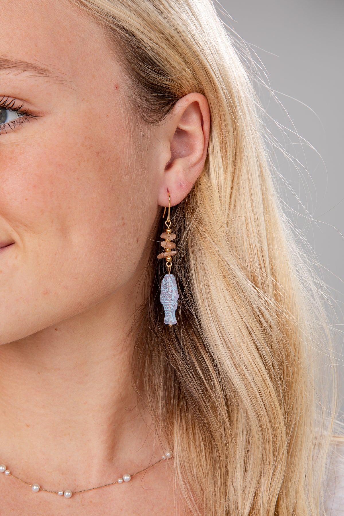 Close-up of a woman wearing a unique earring with a blue gemstone and gold accents.