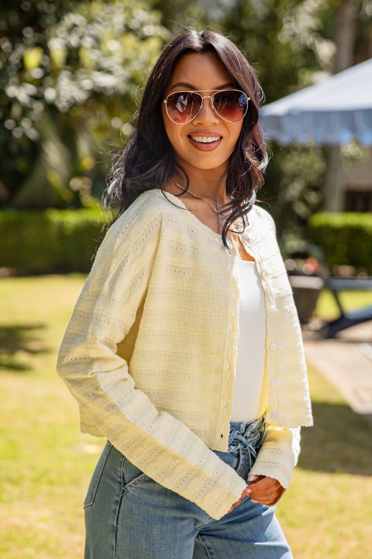 Woman wearing a yellow cardigan, sunglasses, and blue jeans outdoors.