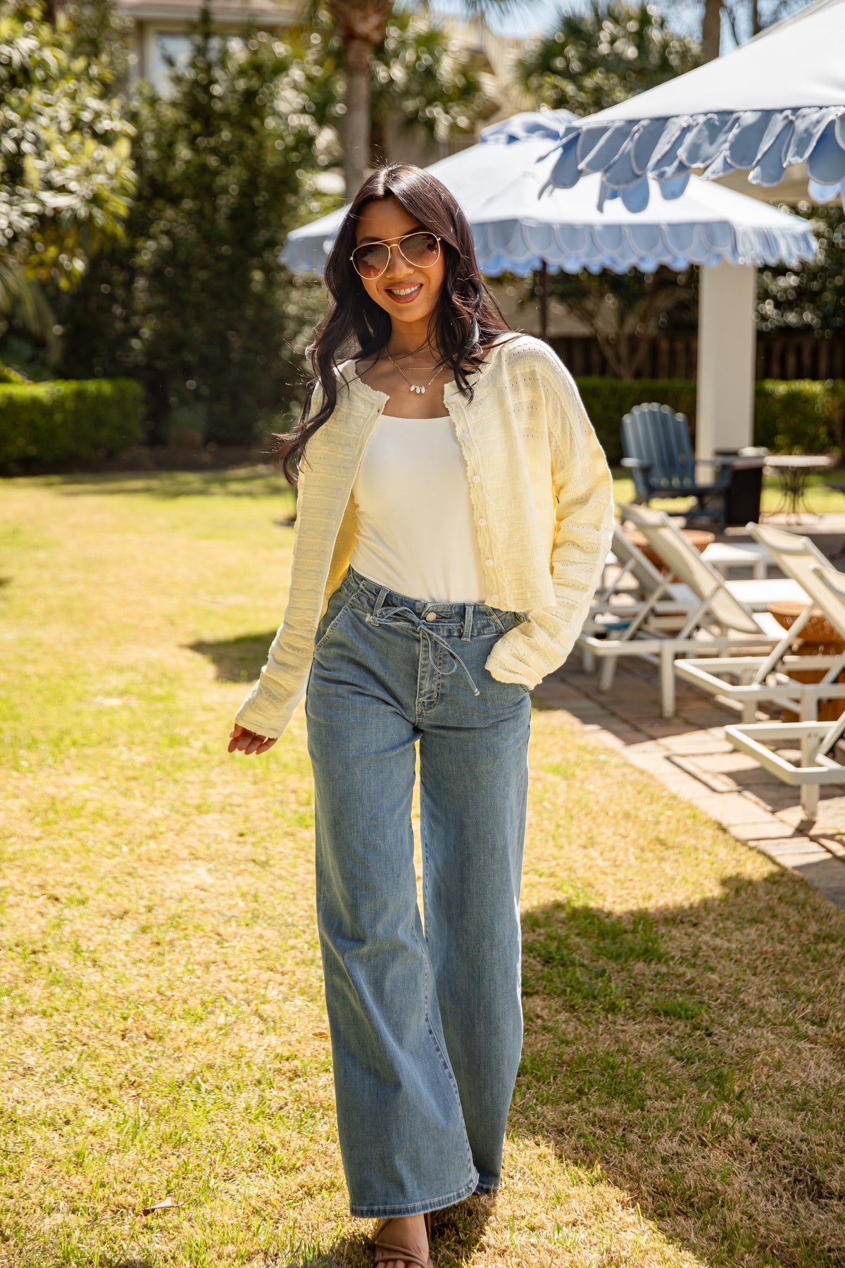 Woman in a yellow cardigan and blue jeans standing outdoors on grass