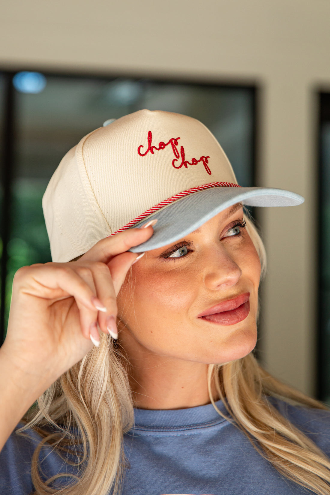 Woman wearing a beige cap with red text, indoors.