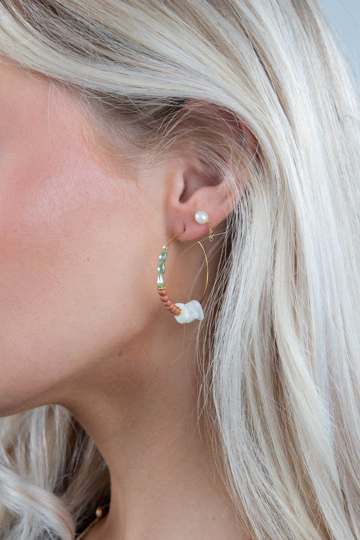 Close-up of a person wearing gold hoop earrings with a neutral background