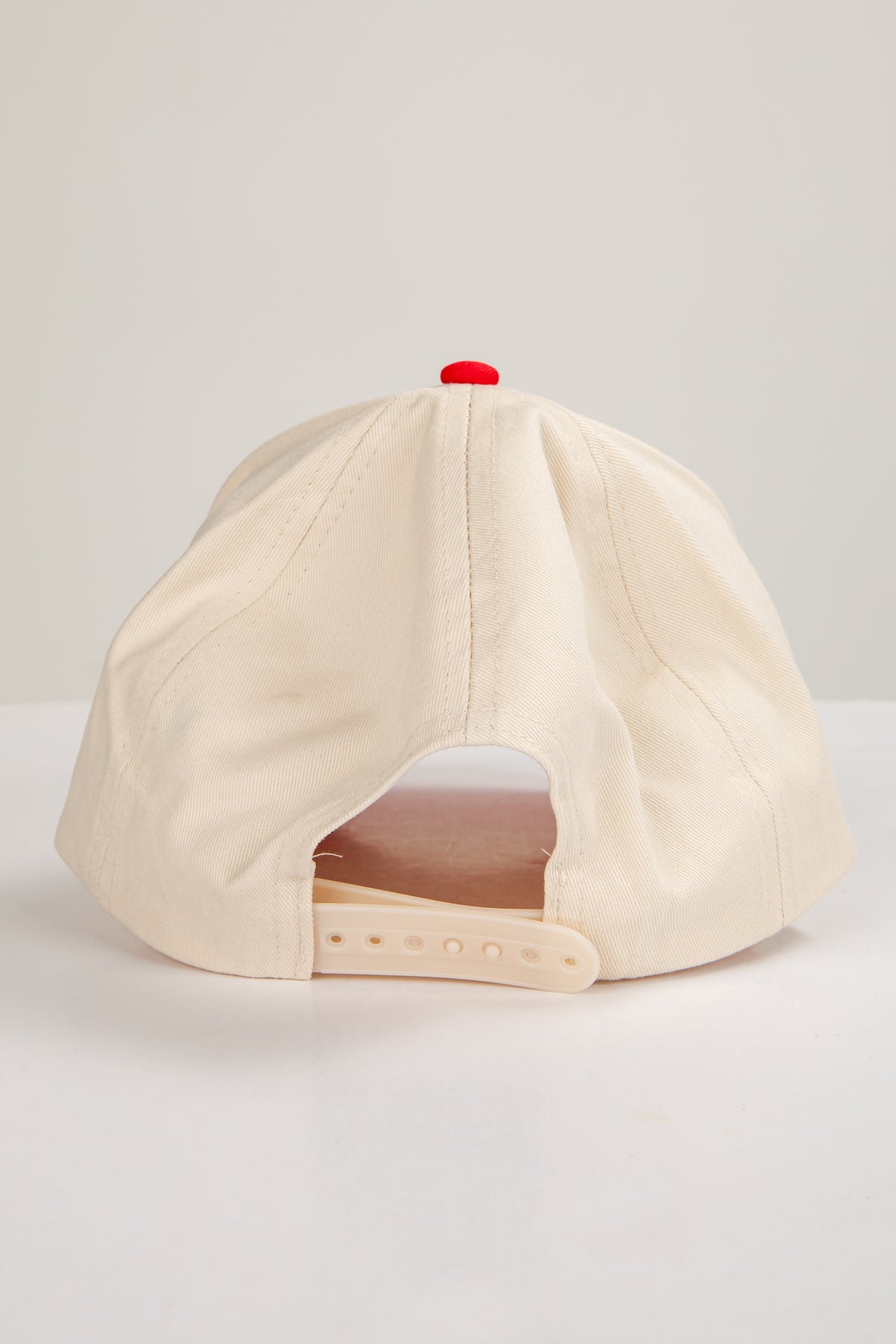 Beige baseball cap with a red button on a light gray background