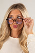 Woman adjusting a pair of sunglasses against a plain background