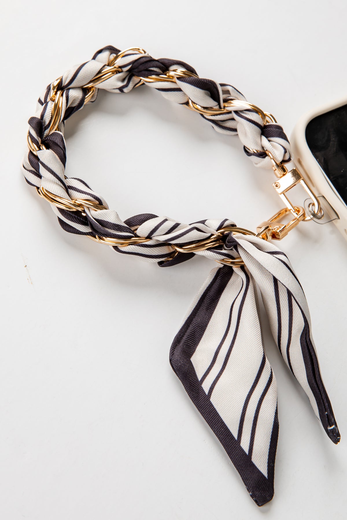 Black and white striped scarf with gold accents draped over a phone on a white background