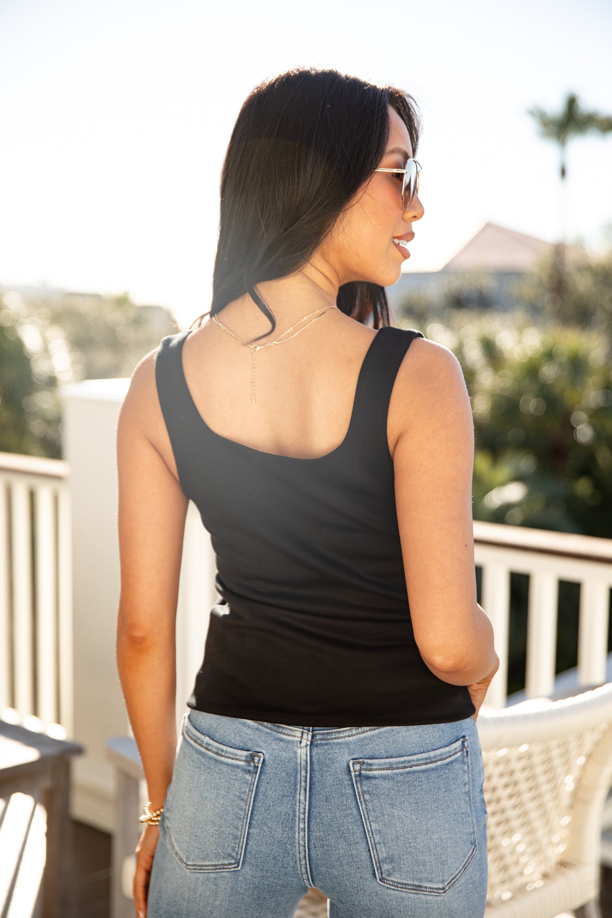 Woman wearing a black tank top and blue jeans standing on a balcony with a blurred background