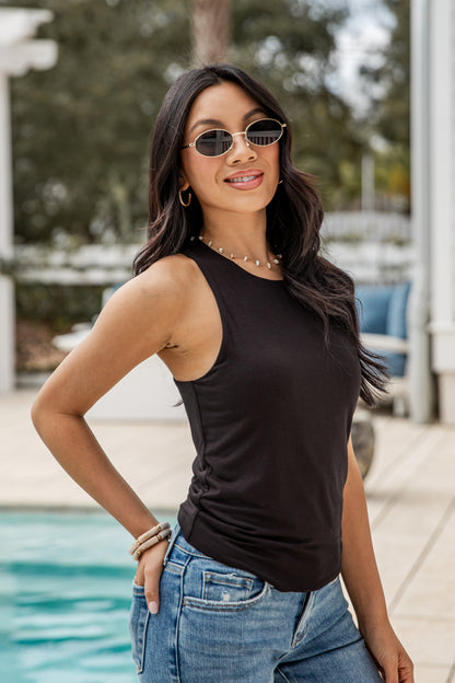 Woman wearing a black tank top and blue jeans by a pool