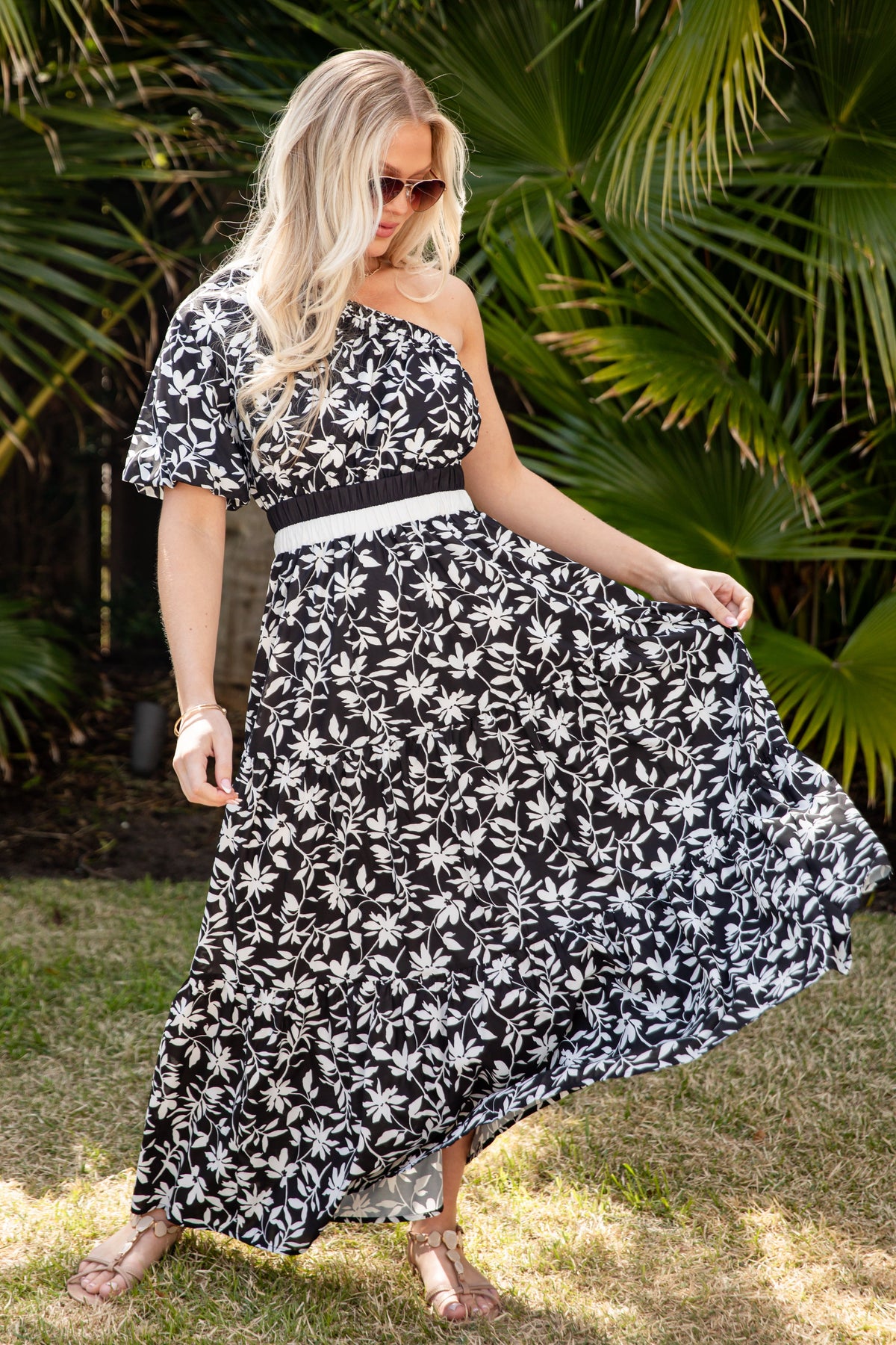 Woman in a black and white floral dress standing outdoors with greenery in the background