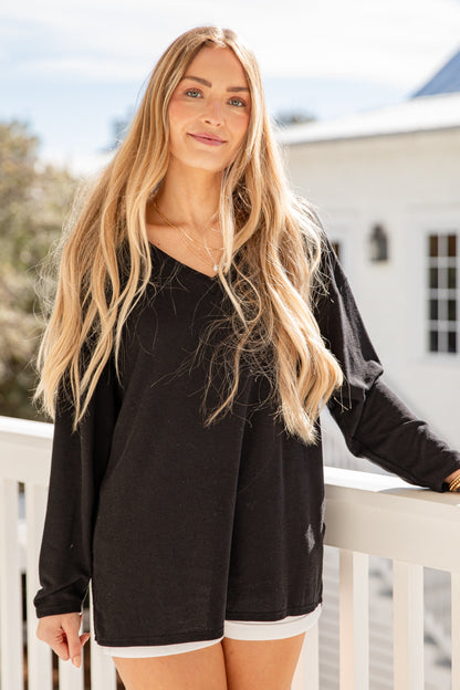 Woman wearing a black long-sleeve top and white shorts on a balcony.