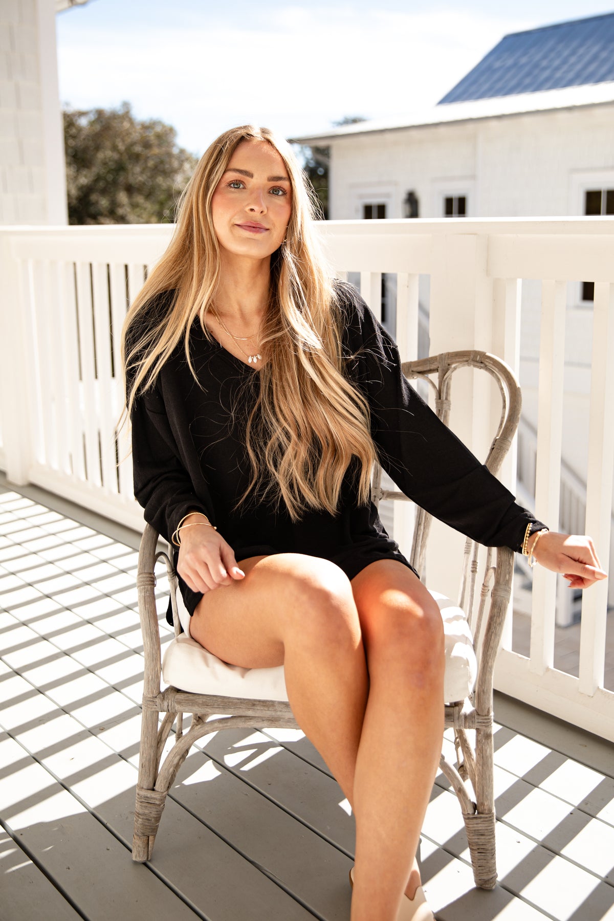 Woman sitting on a chair on a wooden deck with a white railing and building in the background.