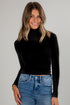 Woman wearing a black turtleneck and blue jeans against a gray background