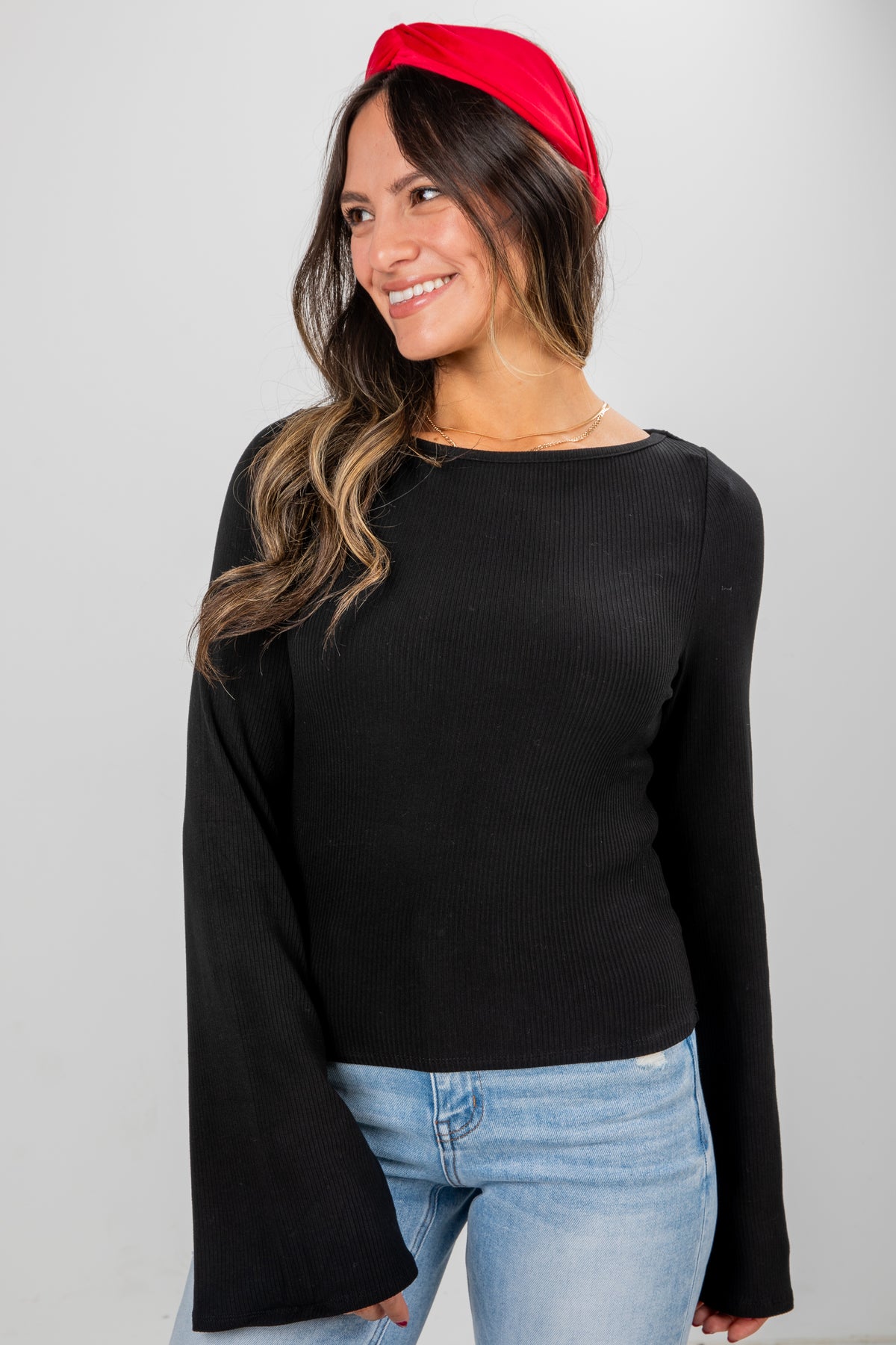 Woman wearing a black long-sleeve top and red headband on a gray background