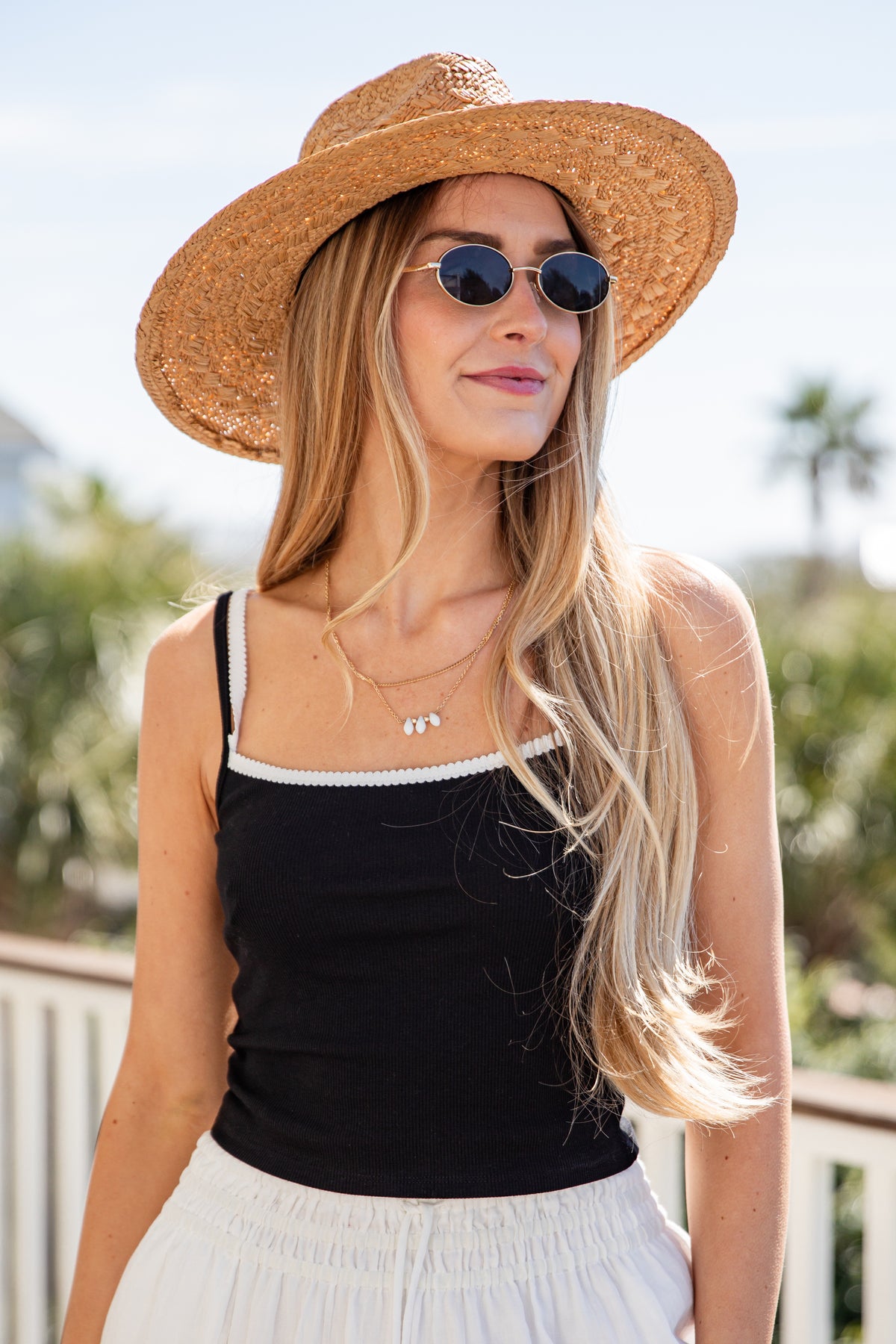 Woman wearing a straw hat, black top, and white pants outdoors.