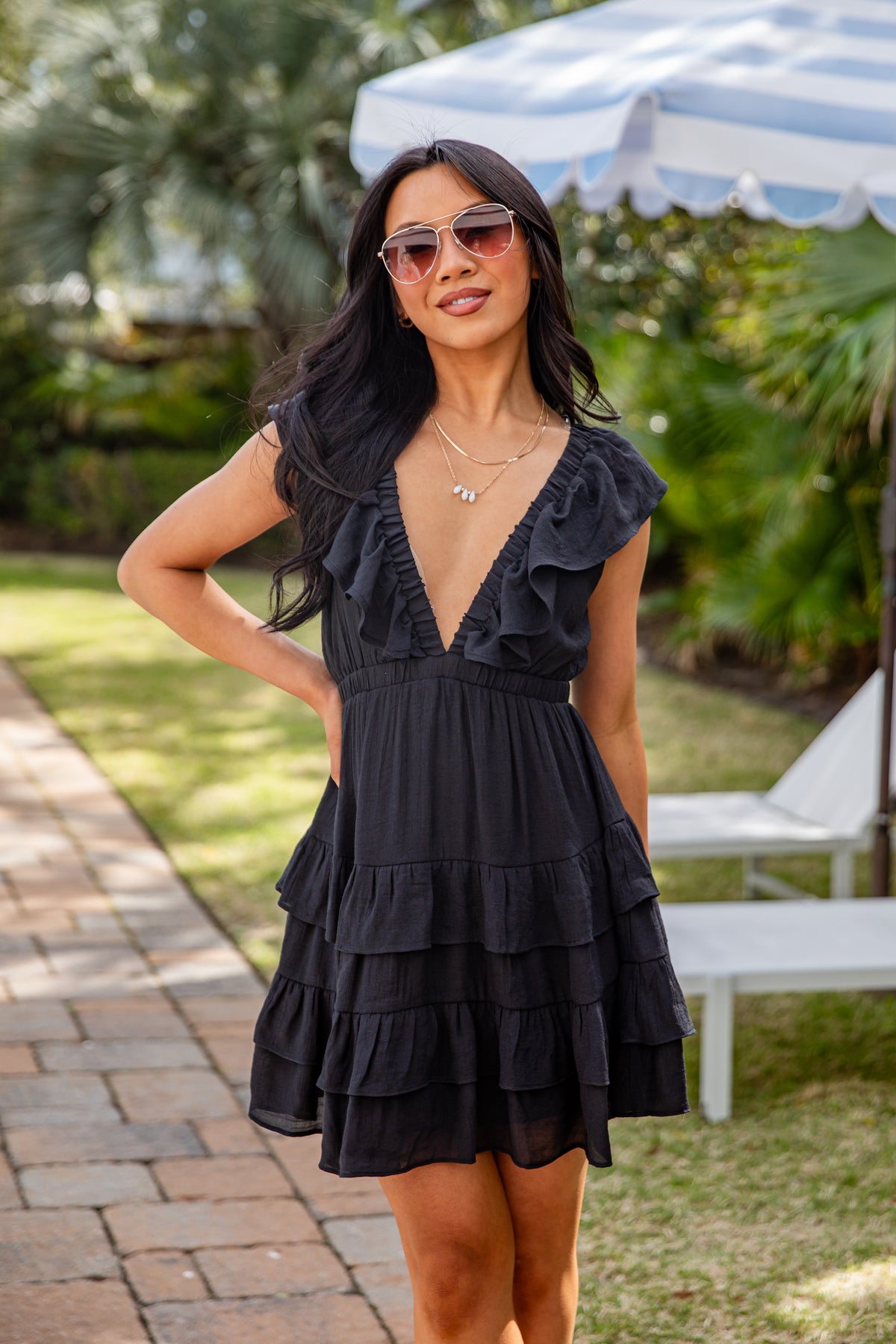 Woman wearing a black ruffled dress with sunglasses outdoors.