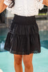 Person wearing a black skirt with lace trim in front of a blurred pool background