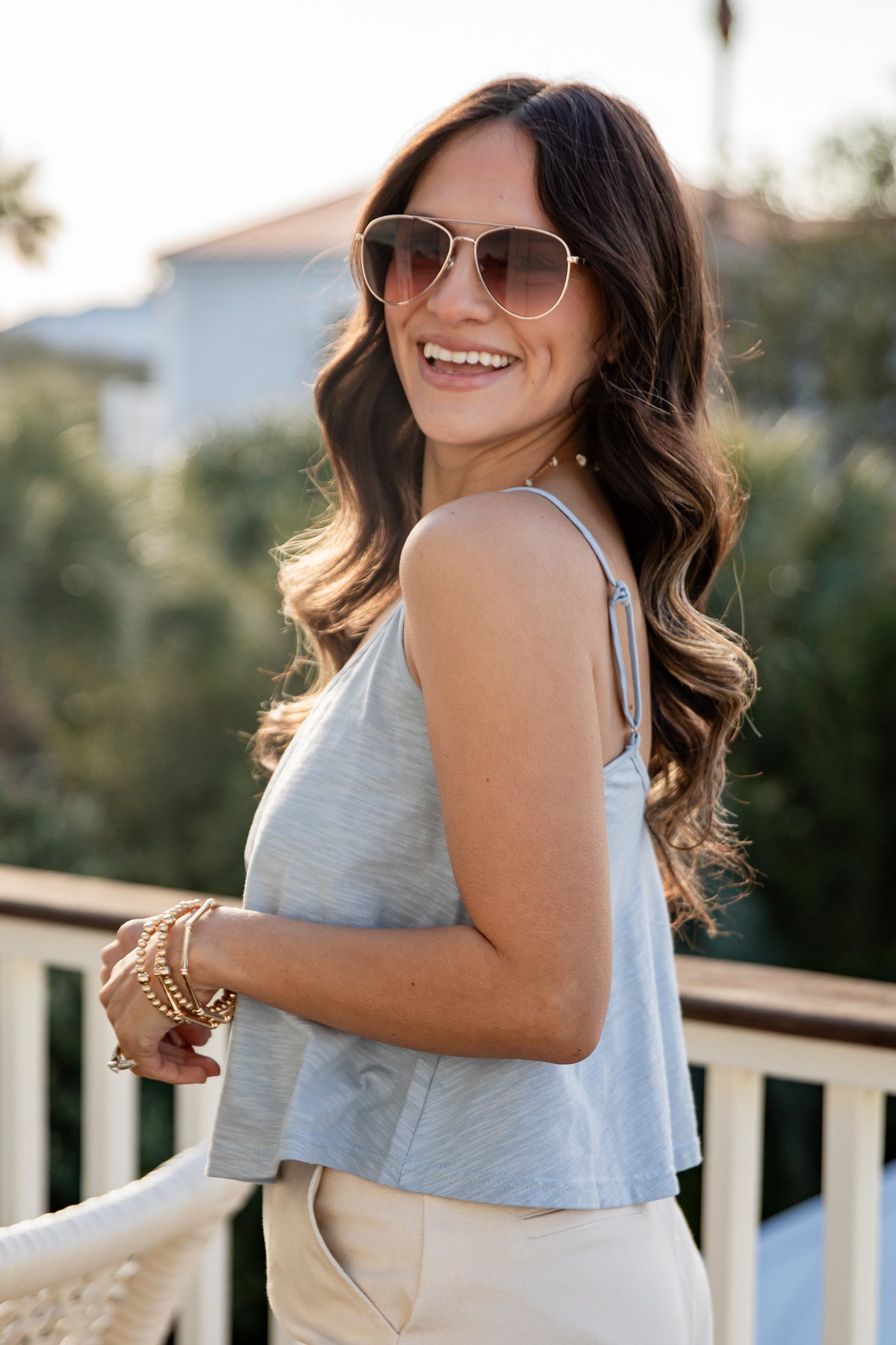 Woman wearing sunglasses and a light blue top with beige pants outdoors.