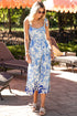 Woman in a blue floral dress standing in an outdoor setting with lounge chairs and umbrellas.