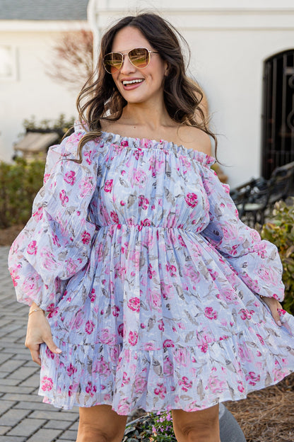 Woman in a floral off-shoulder dress standing outdoors on a brick path.