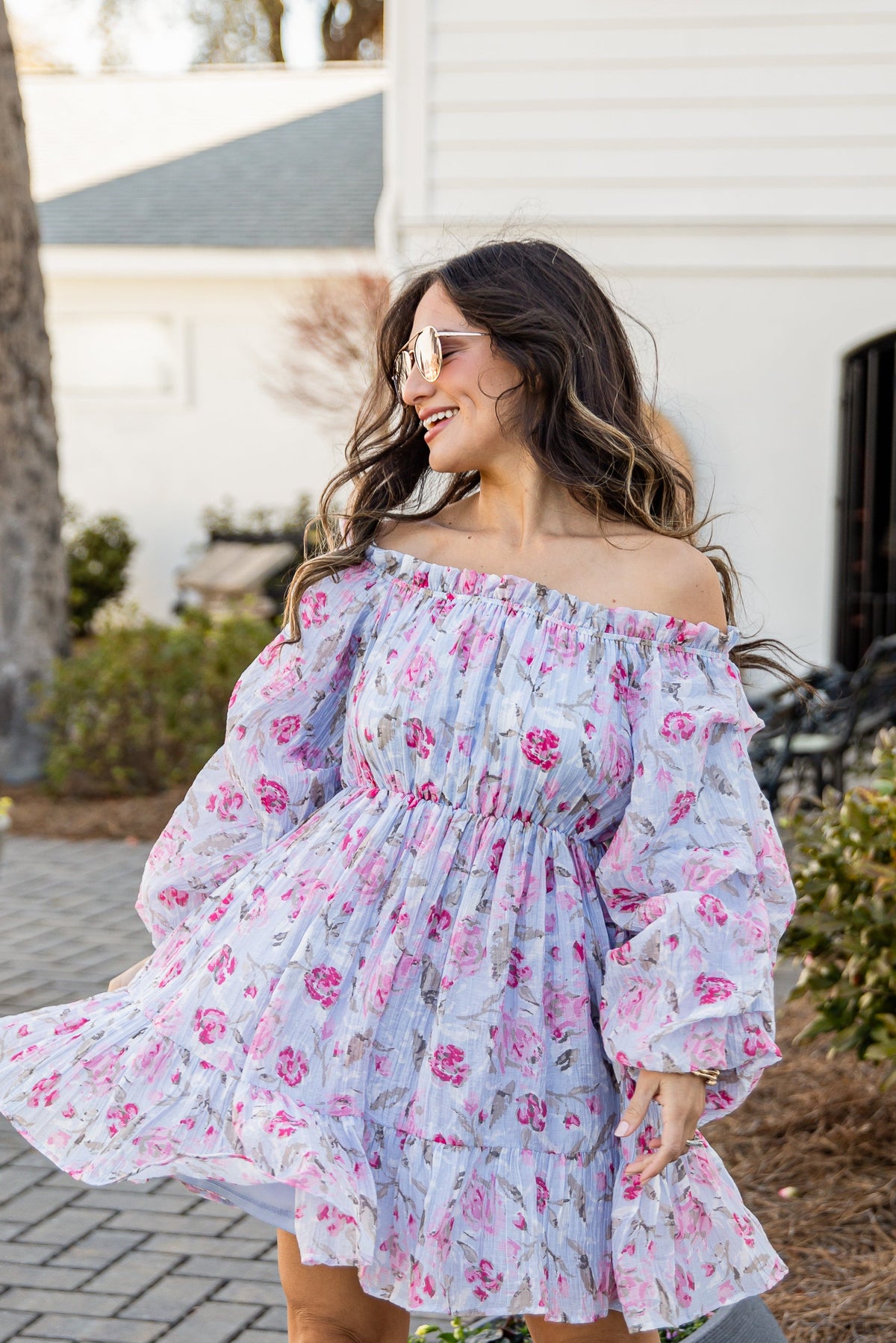 Woman in a floral off-shoulder dress standing outdoors on a patio.