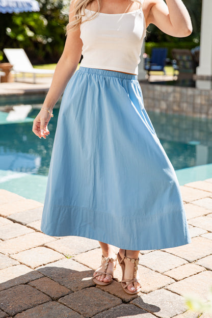 Woman wearing a white top and blue skirt by a poolside