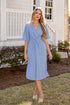 Woman in a light blue dress standing in front of a house.