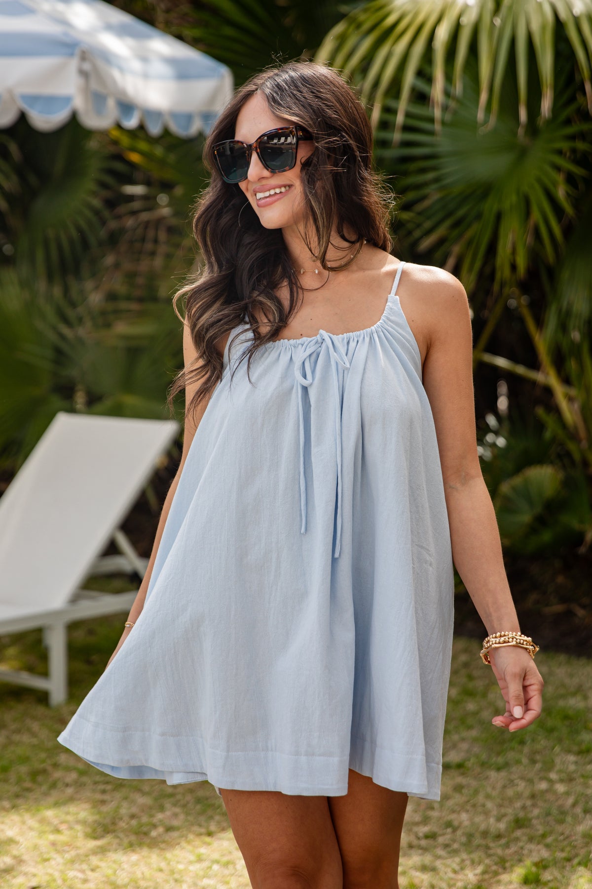 Woman wearing a light blue dress with sunglasses in a garden setting