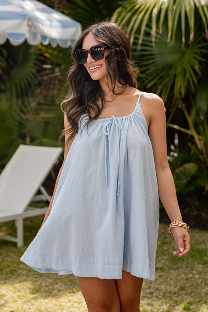 Woman wearing a light blue dress with sunglasses in a garden setting