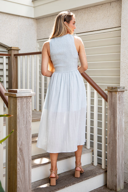 Woman in a light blue dress standing on a staircase with wooden railings.