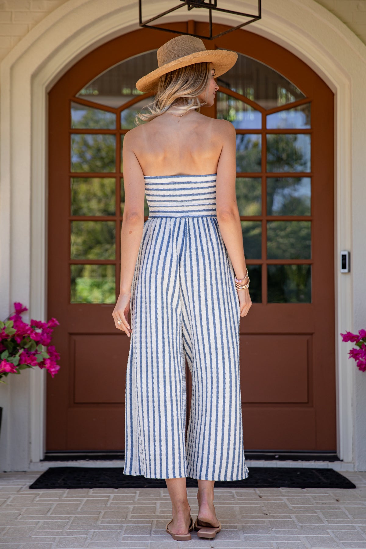 Woman in a striped jumpsuit standing in front of a door with flowers on either side.