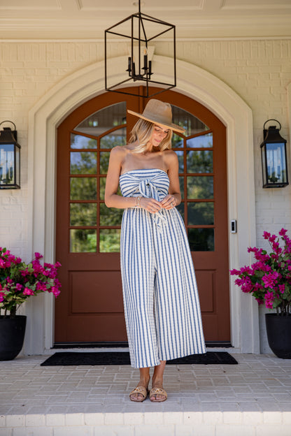Woman in a striped dress standing in front of a house entrance with flowers on either side.