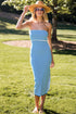 Woman in a blue and white striped dress and sun hat standing on grass with trees in the background