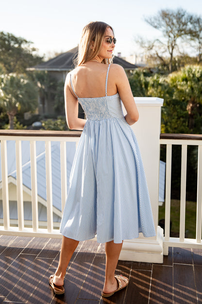 Woman in a blue striped dress standing on a balcony with greenery in the background