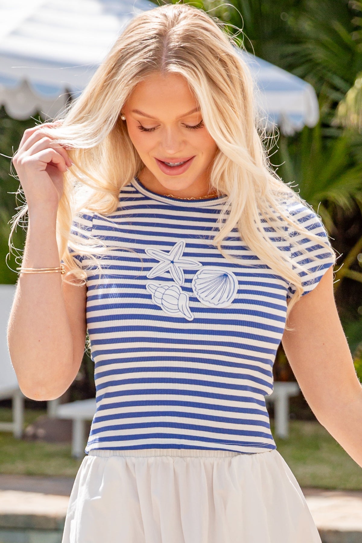 Woman wearing a blue and white striped shirt with a graphic design, standing outdoors near a pool.
