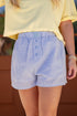 Person wearing a yellow top and blue striped shorts with a blurred background