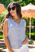 Woman wearing a blue sleeveless top with buttons, smiling outdoors with orange umbrellas in the background.