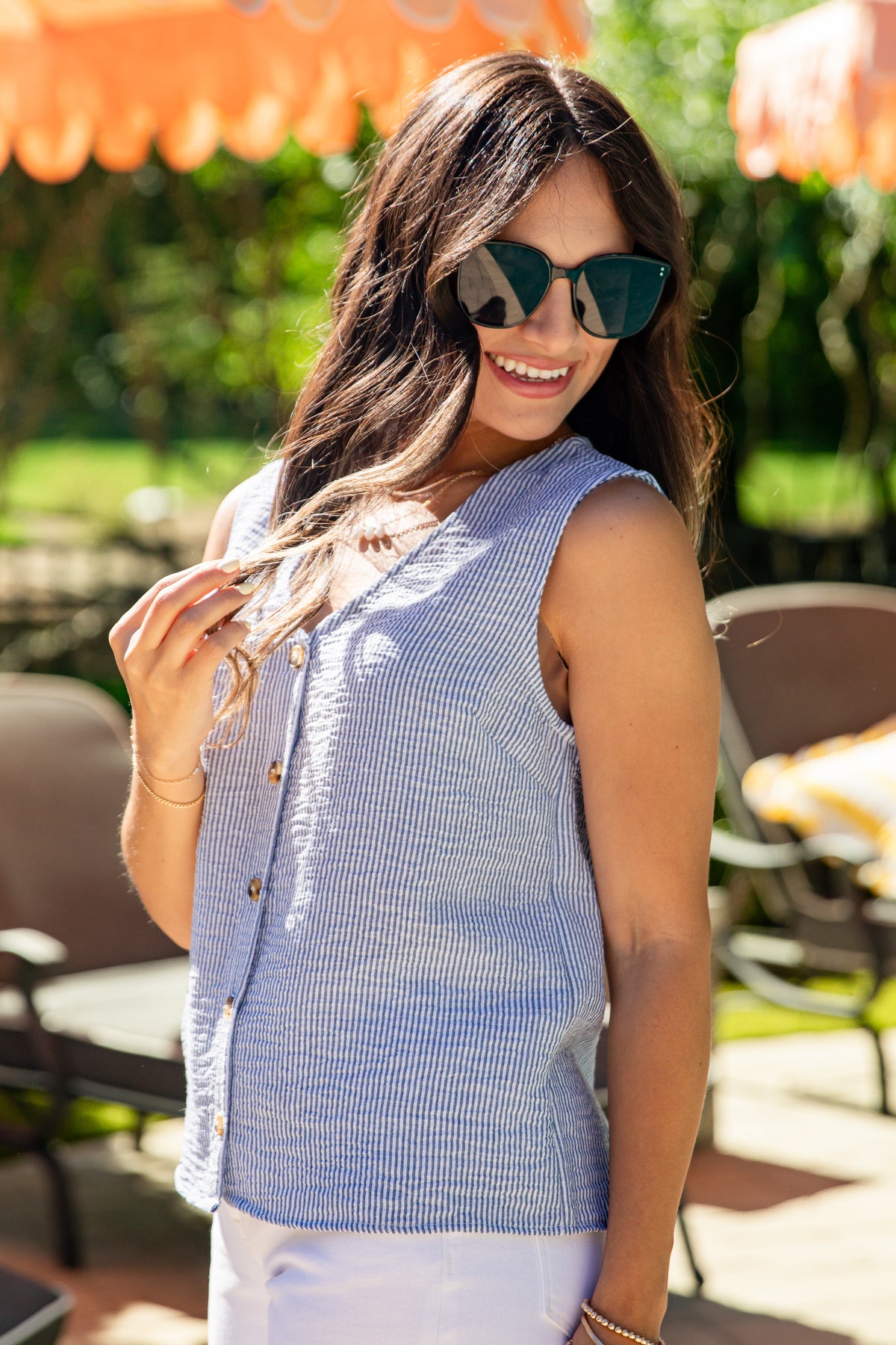 Woman wearing sunglasses and a blue sleeveless top in an outdoor setting