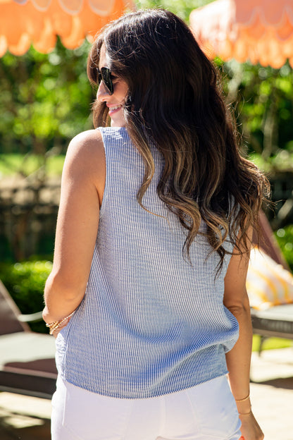 Woman wearing a blue sleeveless top and white pants outdoors