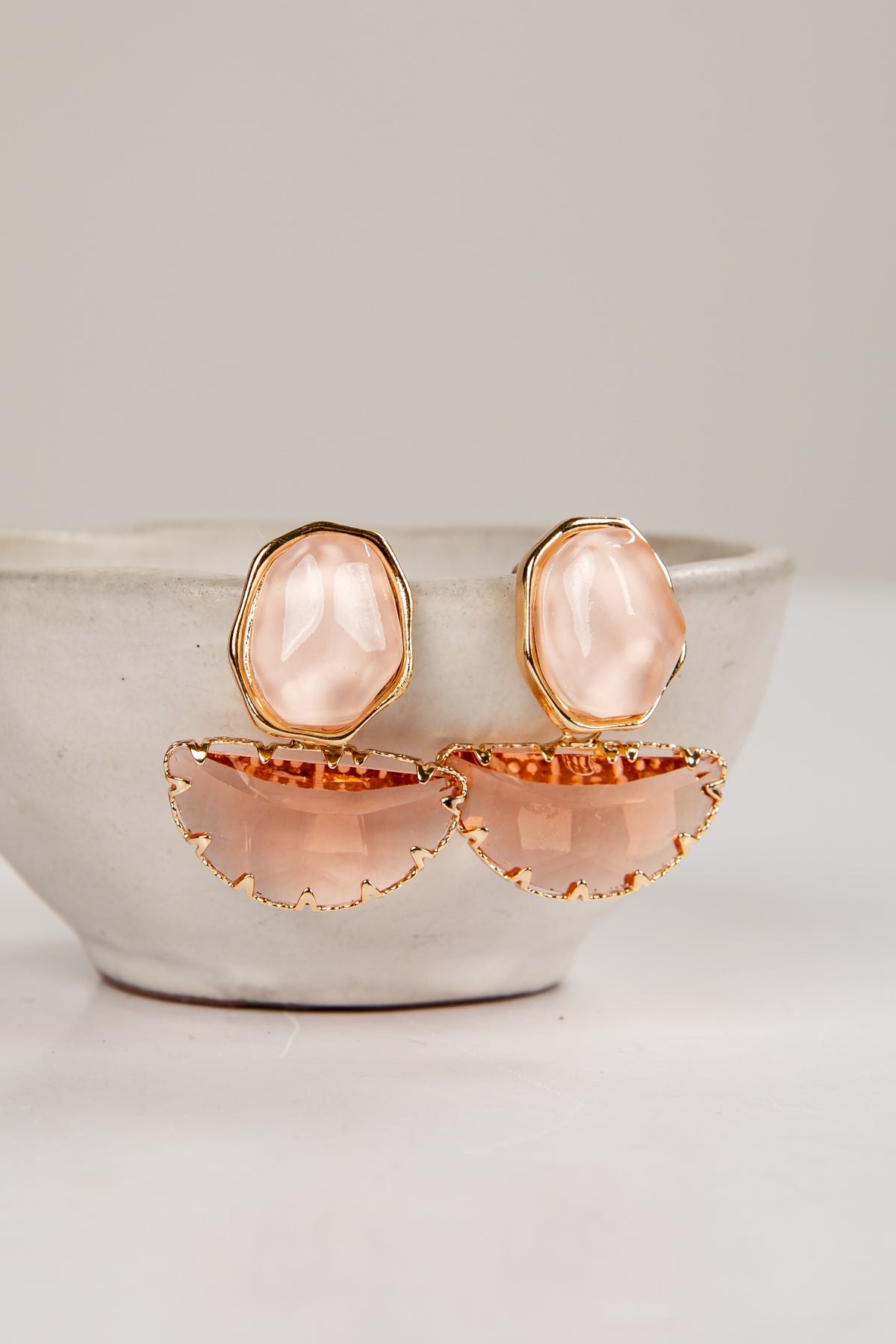 Pair of earrings with pink stones and gold accents on a white surface.