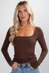 Woman wearing a brown long-sleeve top against a plain background