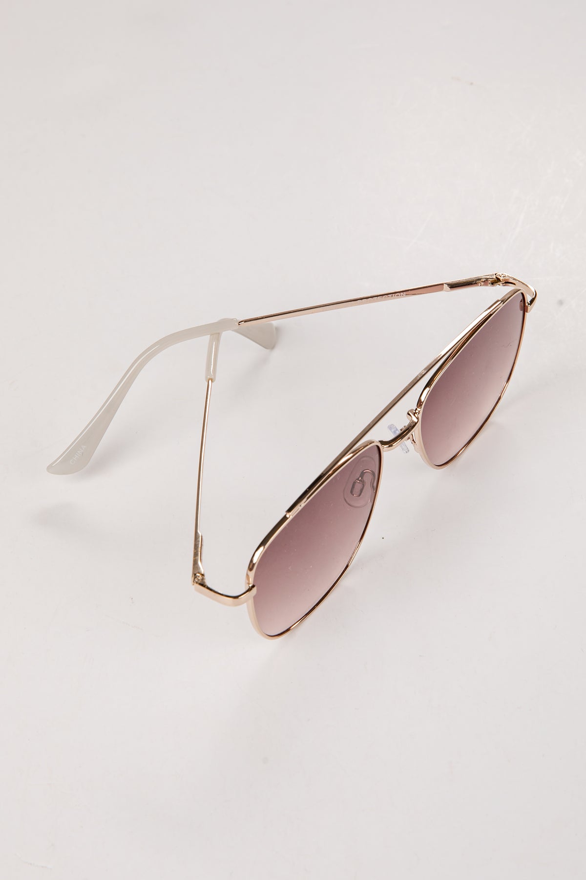 Sunglasses with gold frame and pink lenses on a light gray background