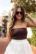 Woman wearing a brown strapless top and white skirt outdoors.