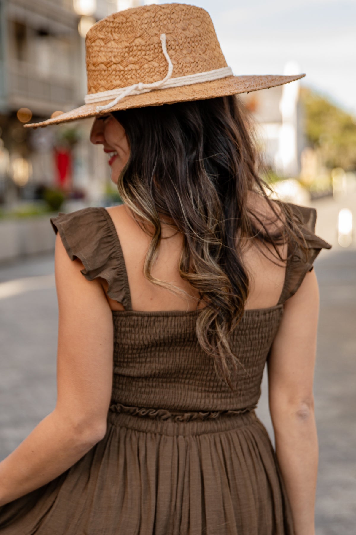 Woman wearing a brown dress and straw hat in an outdoor setting