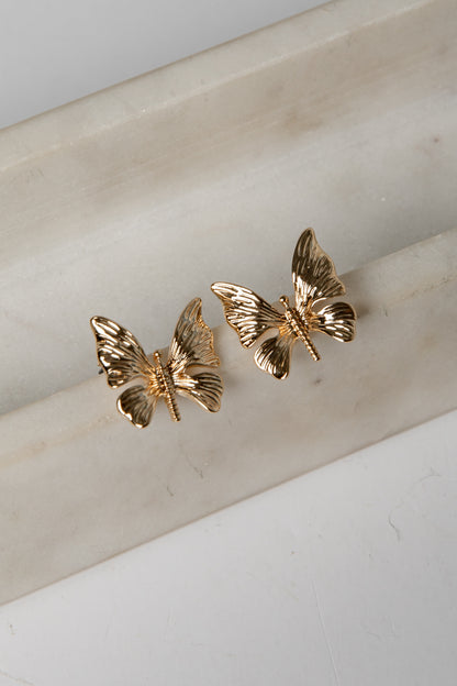 Gold butterfly earrings on a marble surface